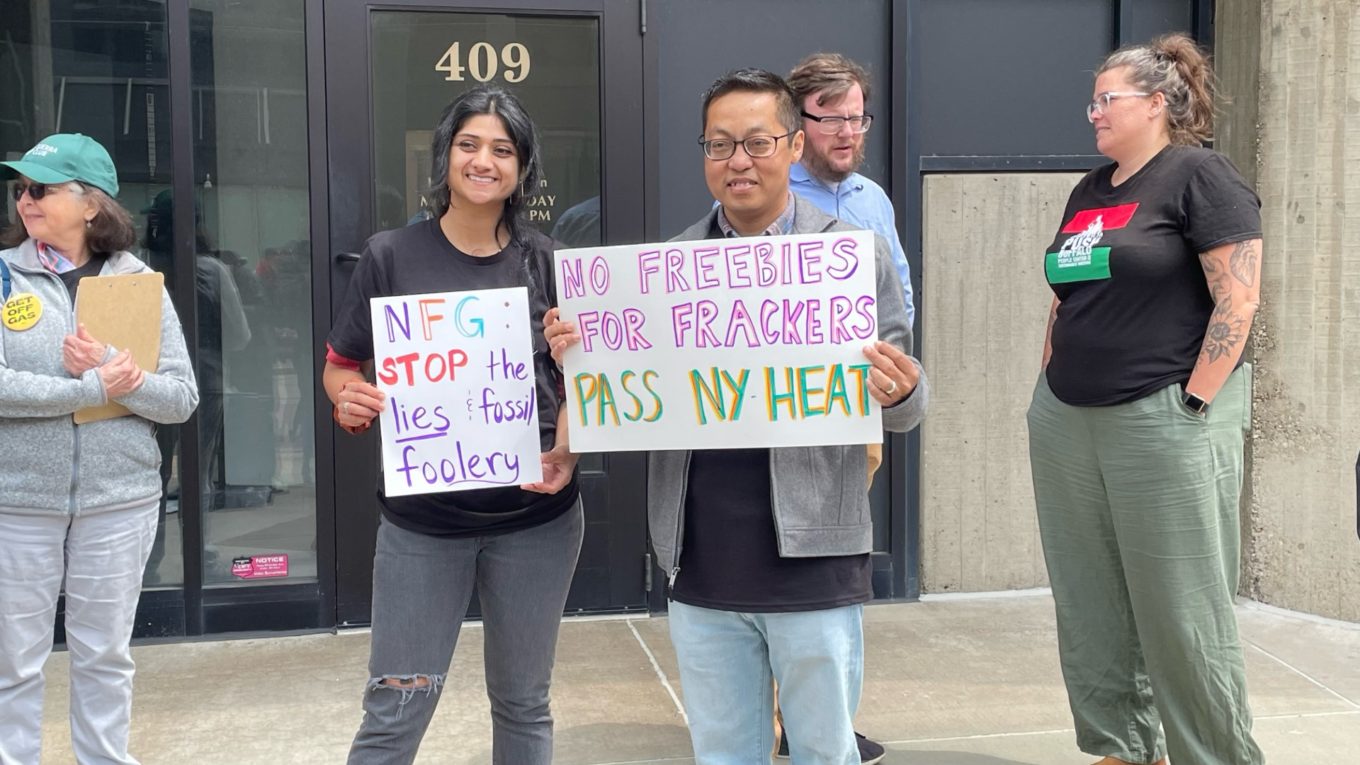 Two people outside of National Fuel Gas' Buffalo offices hold signs that say "NFG: Stop the lies and fossil foolery" and "No Freebies for Frackers. Pass NY HEAT".